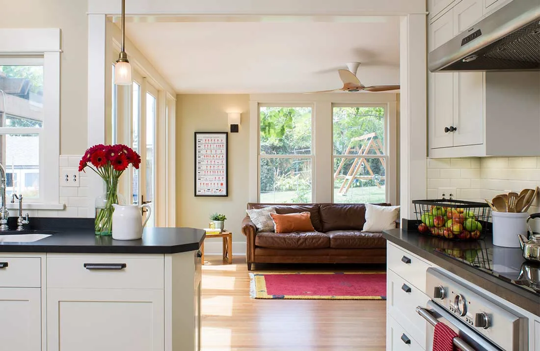 Interior of living room and kitchen with large windows, hardwood floors, grey cabinets, and black countertops.