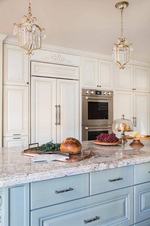 Custom kitchen remodel featuring blue and white cabinetry, brass-accented light fixtures, and stainless steel appliances.