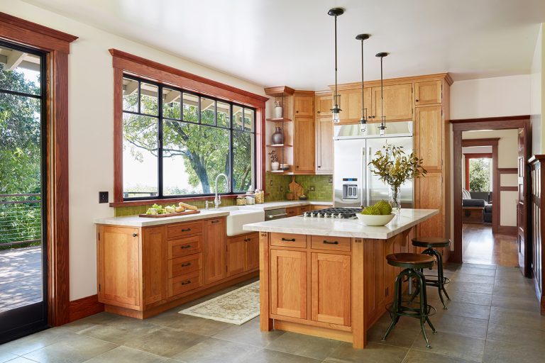 Craftsman home kitchen with fine wood cabinets, marble countertops, and trees out the windows.