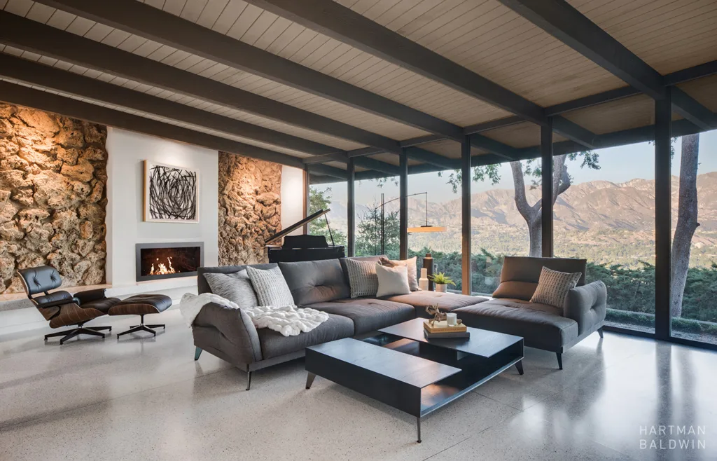 Mid-century modern living room with grey and black furniture, a fireplace, and a mountain range out the window.
