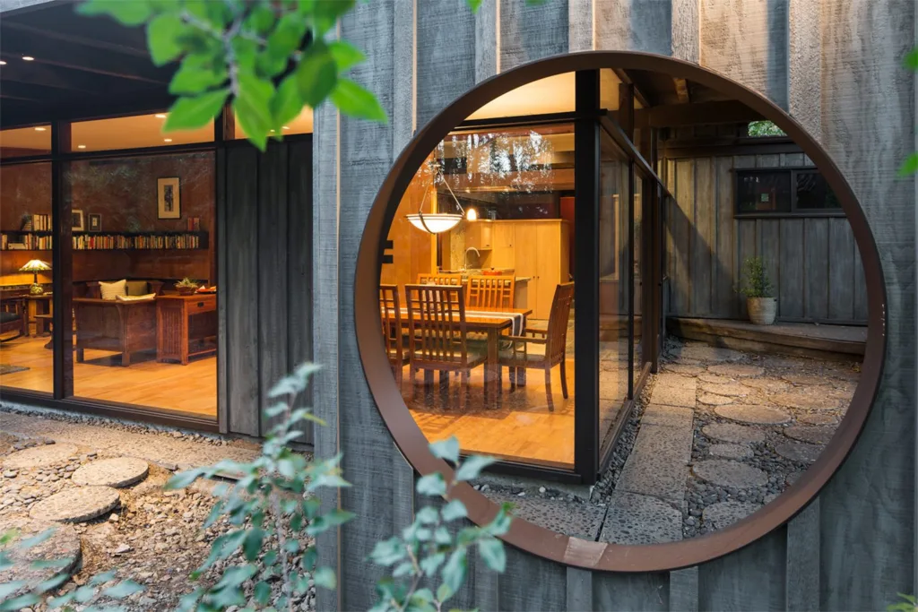 HartmanBaldwin Via Zurita Residence Circular Window and Dining Room - Hartman Baldwin Mid Century Modern Outdoor Design with circular window and large glass windows looking into warmly lit dining room