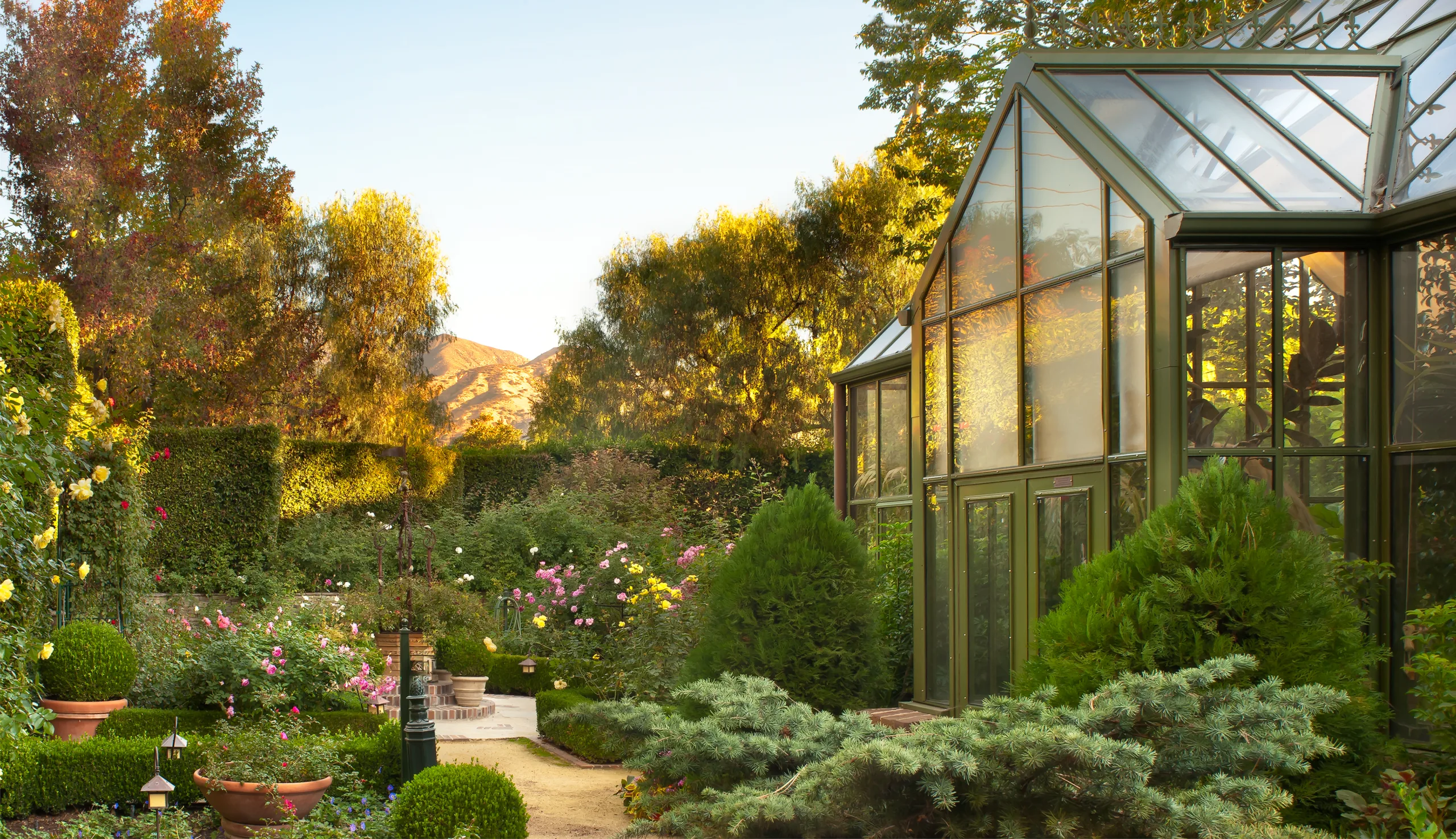 Large glass greenhouse in English-style garden at golden hour