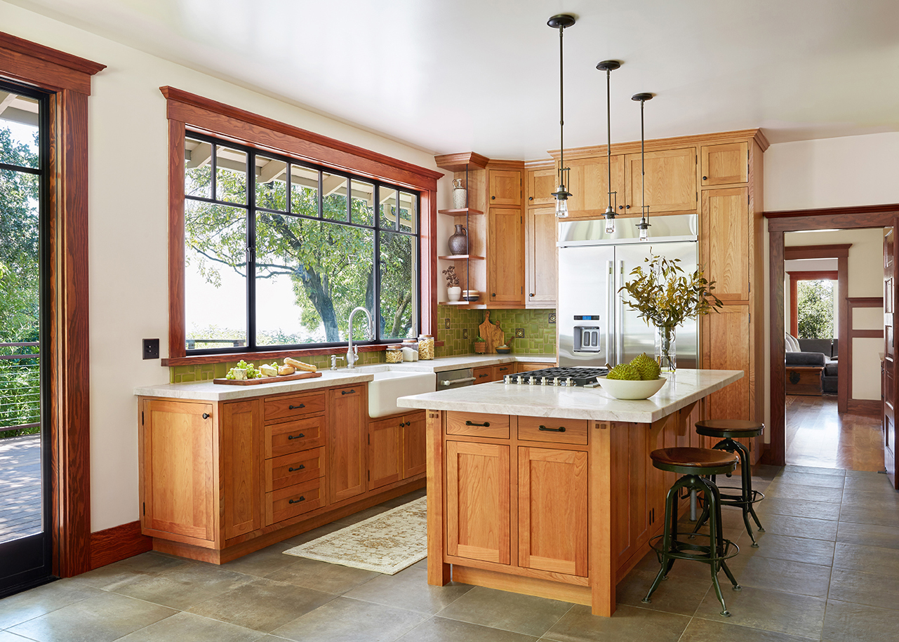 Craftsman home kitchen with fine wood cabinets, marble countertops, and trees out the windows.