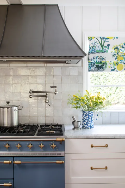 Cape Cod coastal-inspired kitchen detail with Blue French Lacanche range, textured zellige backsplash tile, and aged brass hardware