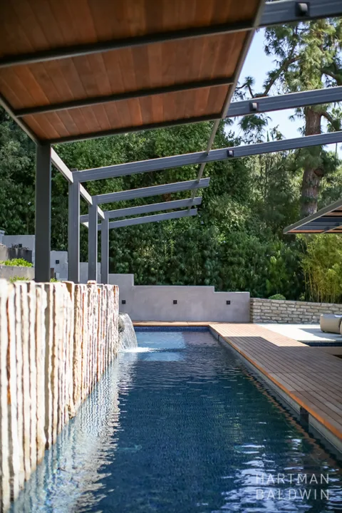 HartmanBaldwin San Rafael Residence Zen Inspired Lap Pool - Hartman Baldwin New luxury backyard lap pool with rock wall installation, waterfall, and retractable shade structure