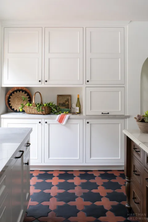 HartmanBaldwin Ledgewood Residence Spanish Style Cabinetry - Hartman Baldwin Functional white cabinetry in new Spanish style kitchen with contrasting red and black patterned terracotta floor