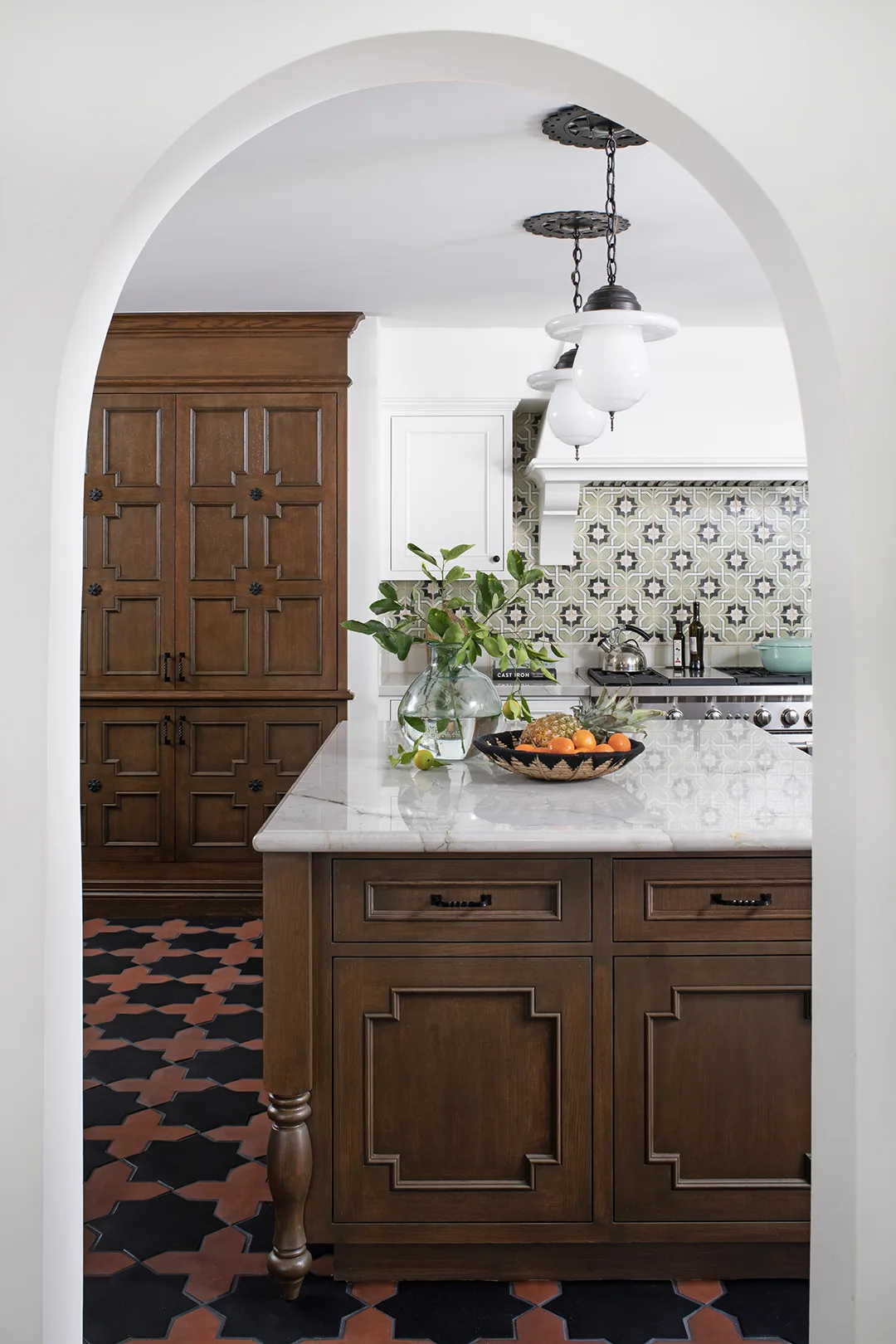 Spanish-style kitchen with colorful geometric tile, dark-stained woodwork, and wrought iron accents seen through arched doorway