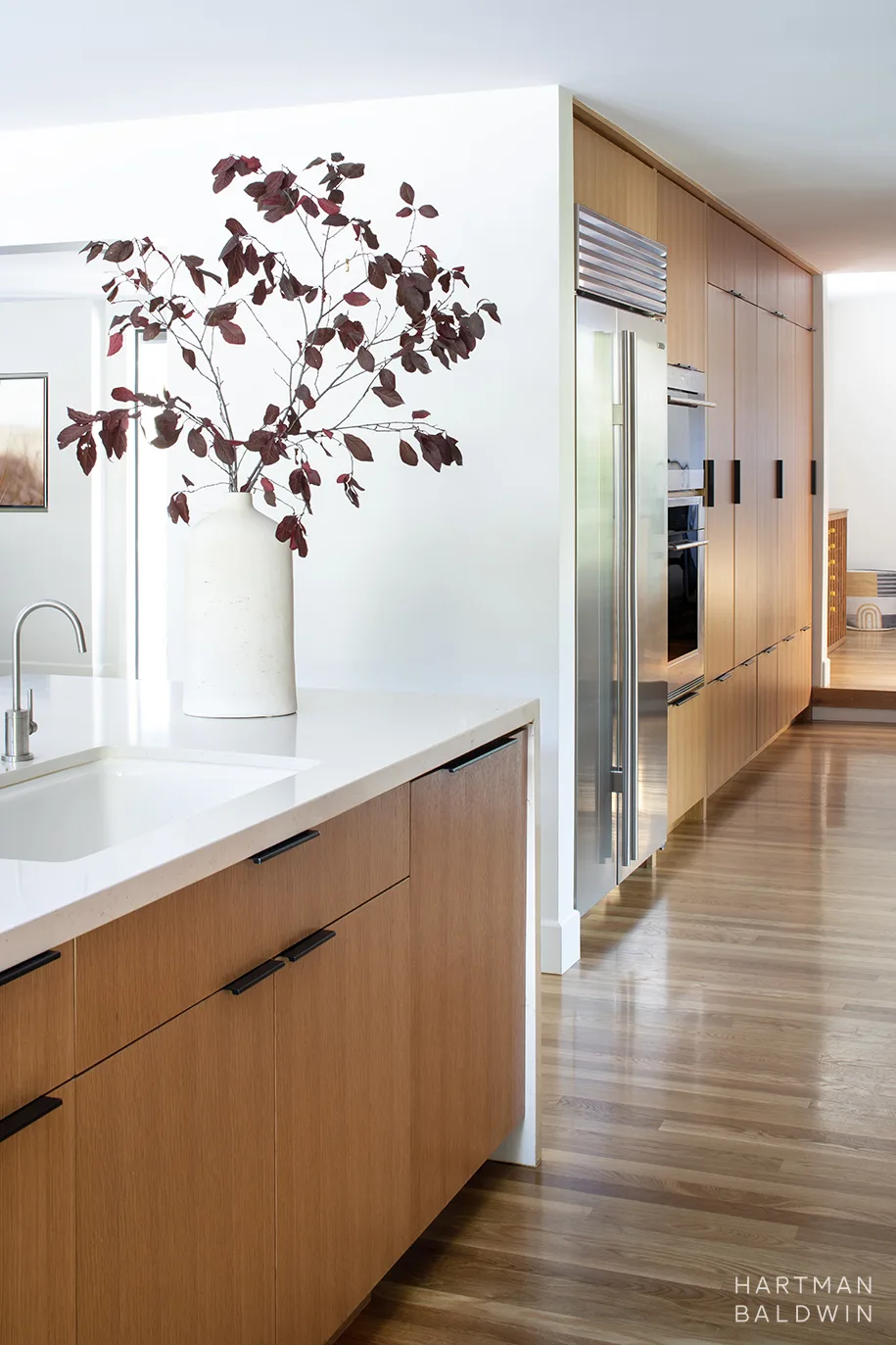 Mid-Century Modern kitchen renovation slab-style oak cabinetry and waterfall-edge island. Large appliances and pantry storage are out of sight but within reach along adjacent hallway