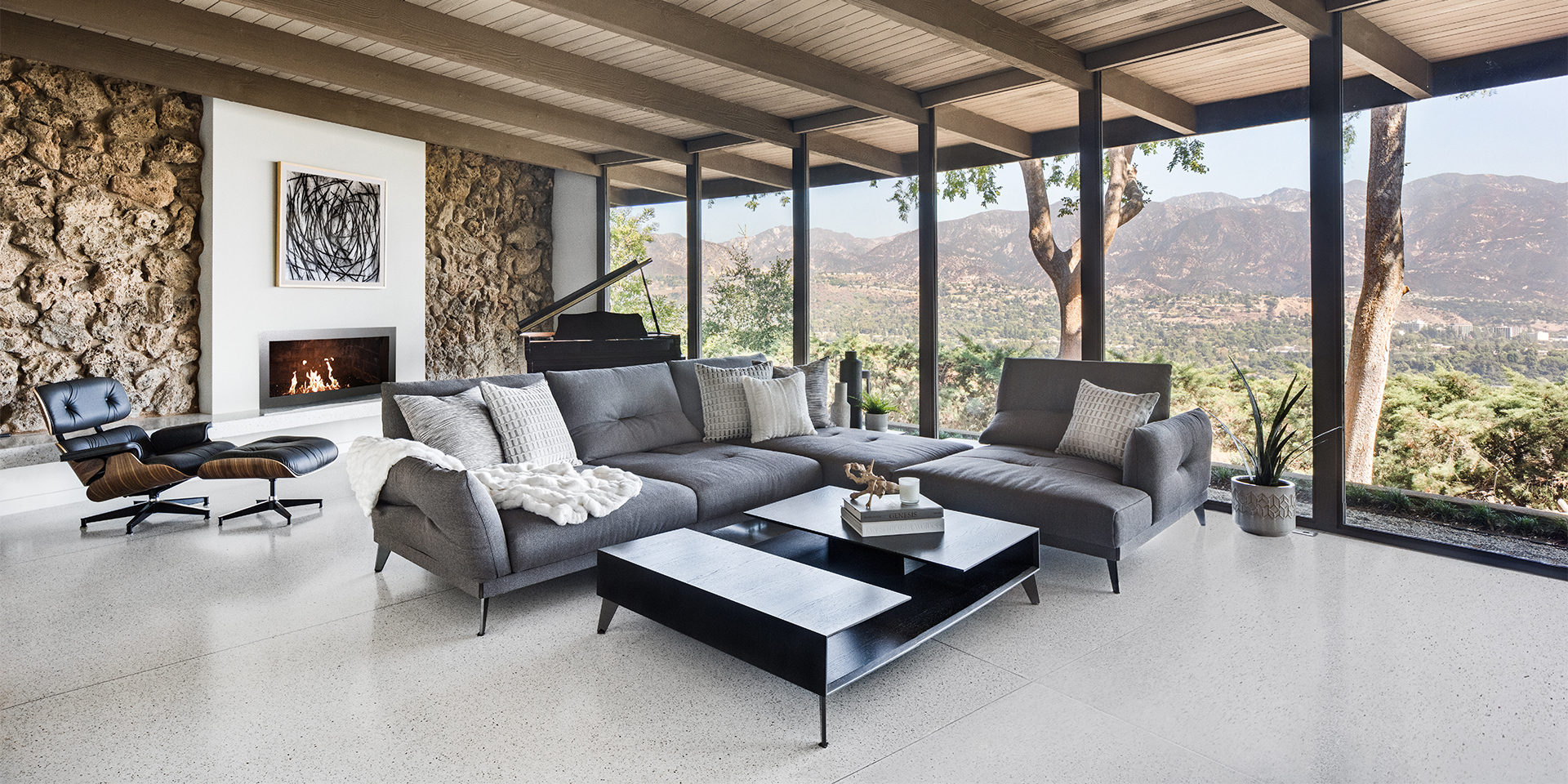 Mid-century modern living room with grey and black furniture, a fireplace, and a mountain range out the window.