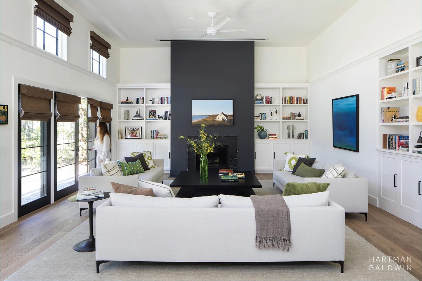Expansive great room with built-in bookshelves, wall-to-wall French doors, comfortable contemporary couches, and floor-to-ceiling navy blue and black stone fireplace