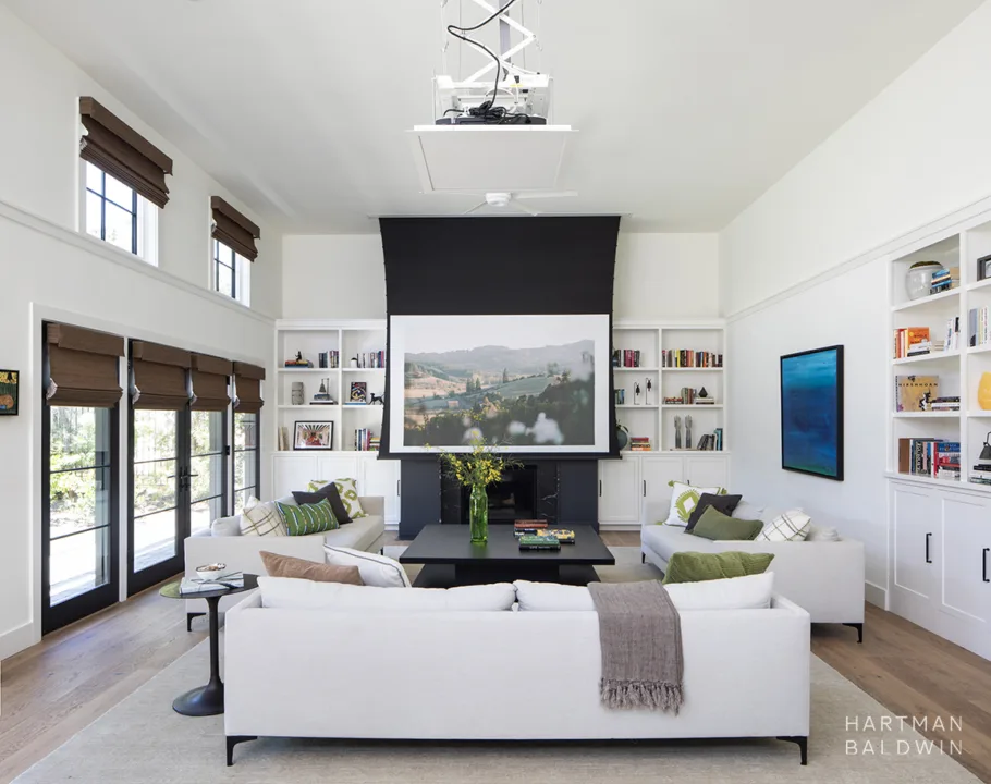 HartmanBaldwin Barrington Residence New Custom Modern Farmhouse Living Room Projector - Hartman Baldwin Expansive great room with built-in bookshelves, wall-to-wall French doors, comfortable contemporary couches, and a retractable projector screen