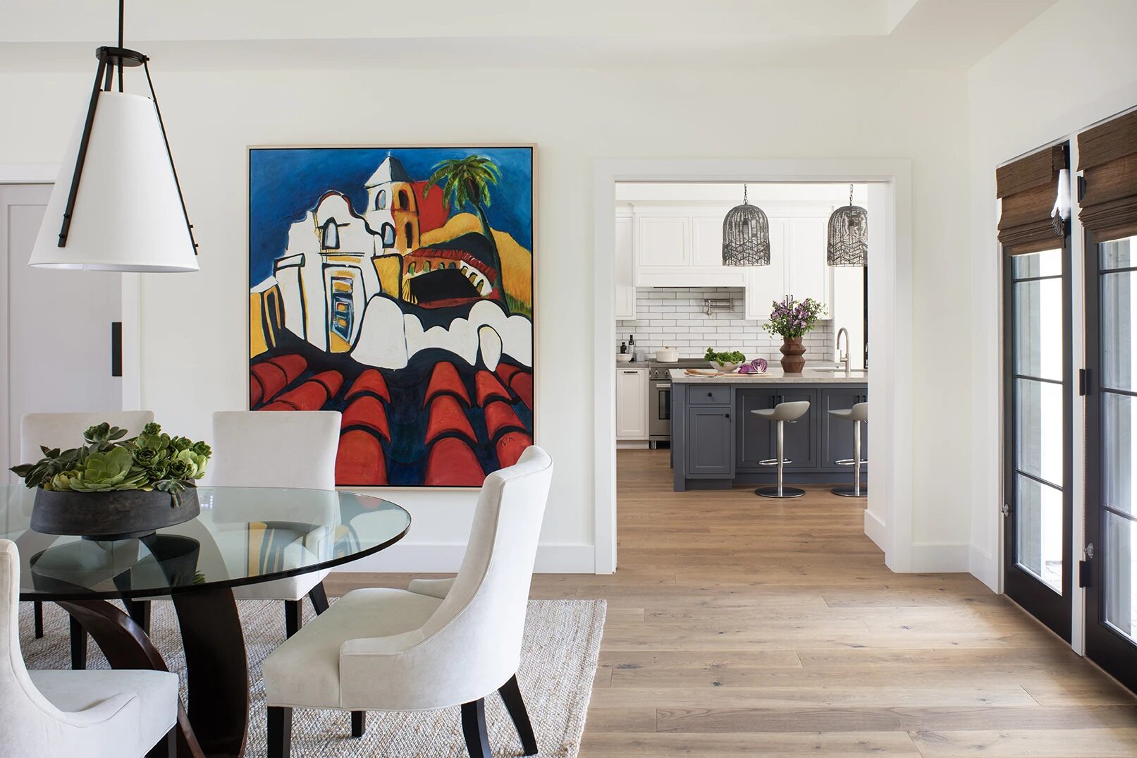 New custom modern dining room with a large colorful painting on the wall and the kitchen with white and blue cabinetry seen beyond