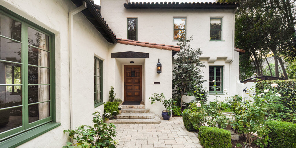 California Spanish-style front porch and courtyard with cream stucco walls, red tile roof, and green-painted trim