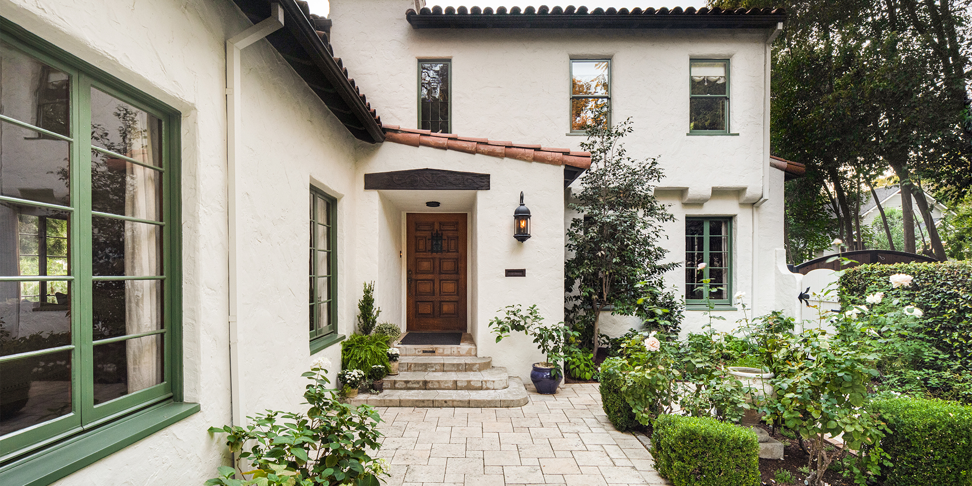 California Spanish-style front porch and courtyard with cream stucco walls, red tile roof, and green-painted trim