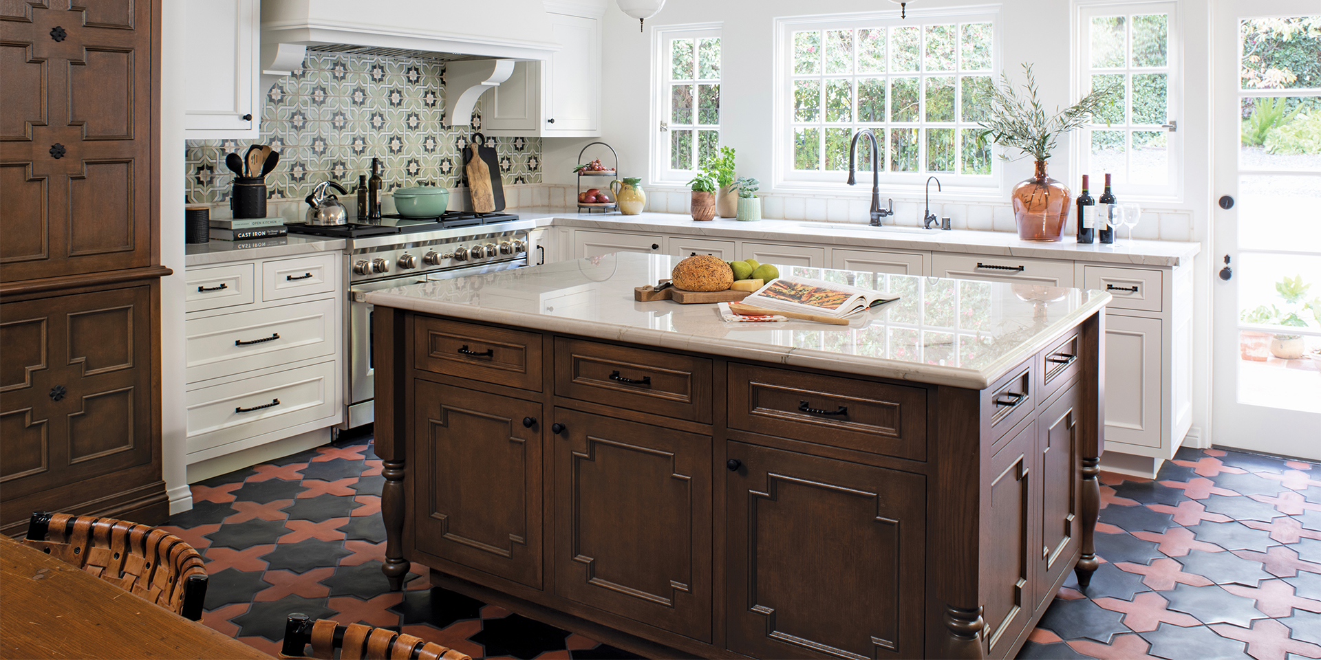 Remodeled Spanish-style kitchen with colorful geometric floor and backsplash tile, dark-stained furniture-style island and pantry, and bright white perimeter cabinetry