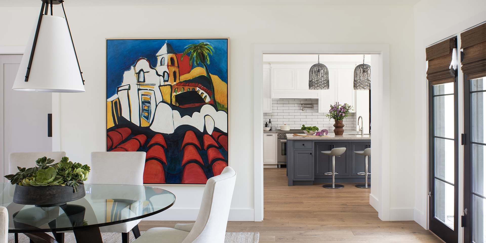 New custom modern dining room with a large colorful painting on the wall and the kitchen with white and blue cabinetry seen beyond