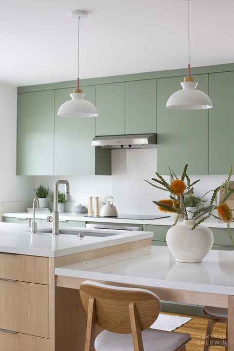 Contemporary Scandinavian minimalist style kitchen remodel with sage green cabinetry, sculptural pendant lights, and central island with built-in dining table