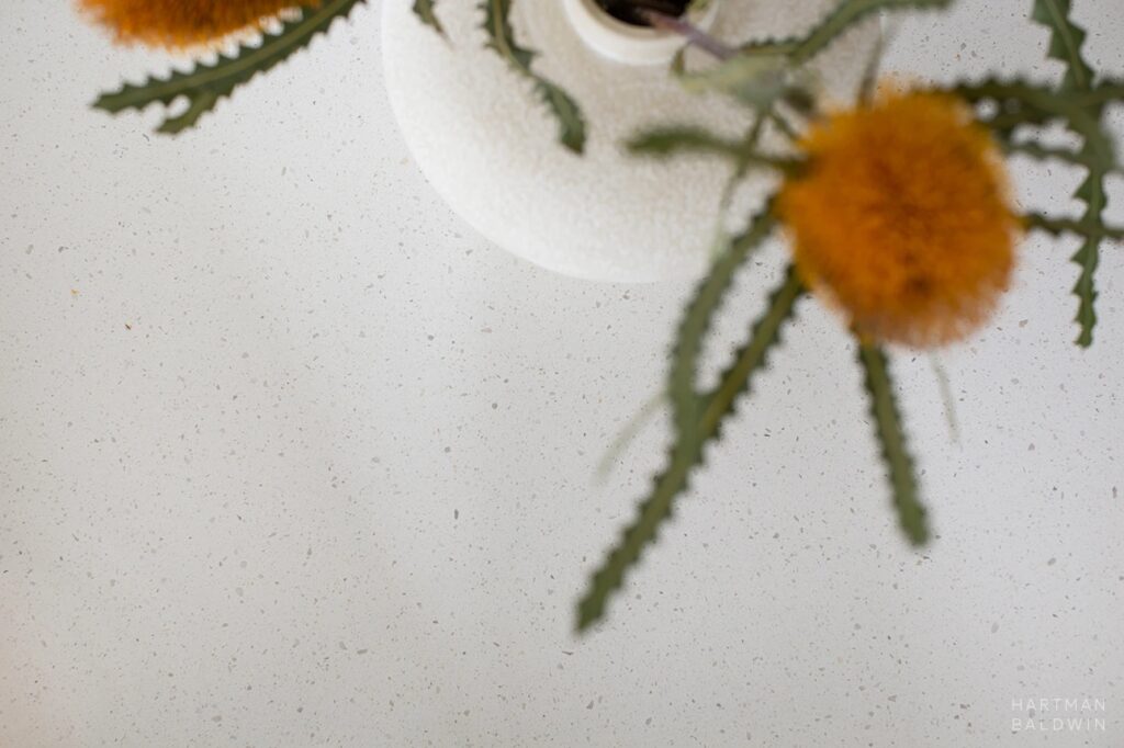 Unique spiky orange flowers in white ceramic vase on light-colored speckled quartz countertop