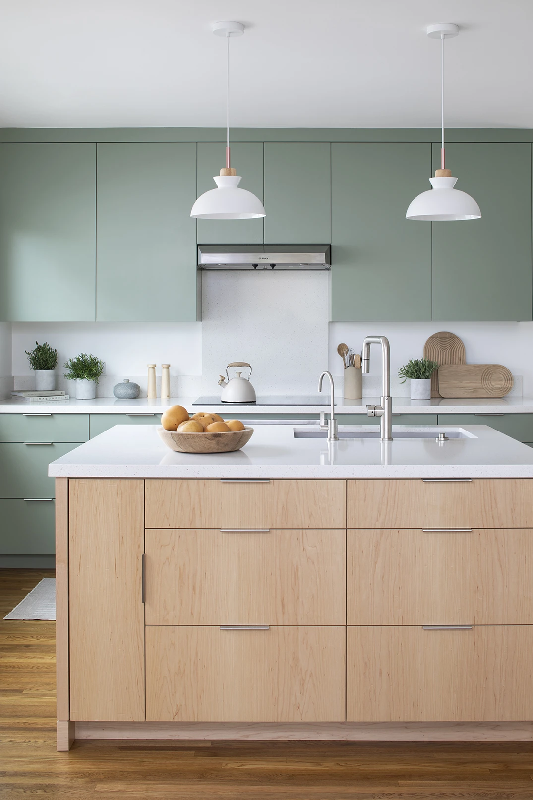 Scandinavian minimalist-style remodeled kitchen with sage green painted cabinetry, sculptural pendant lights, and multifunctional light maple island with a white quartz countertop