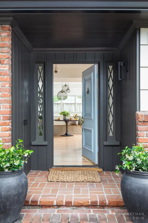 Remodeled front porch with red brick exterior, dark grey painted wood paneling, and blue front door open to entryway and breakfast nook inside