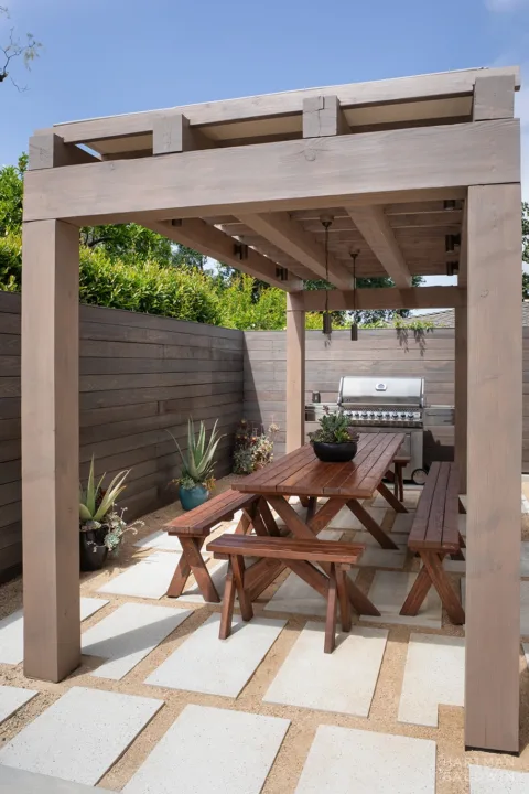 Backyard wooden shade structure with picnic table, cement pavers, and stainless steel barbecue