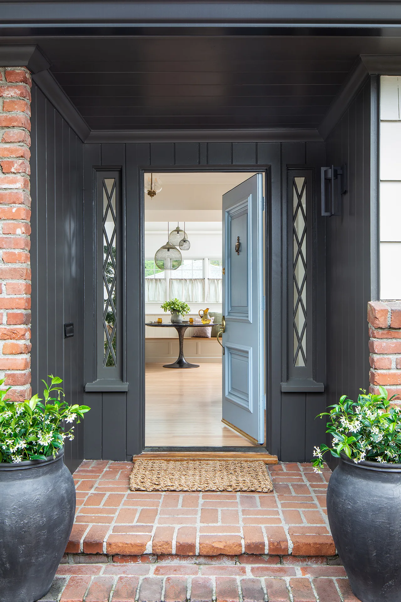 Remodeled front porch with red brick exterior, dark grey painted wood paneling, and blue front door open to entryway and breakfast nook inside