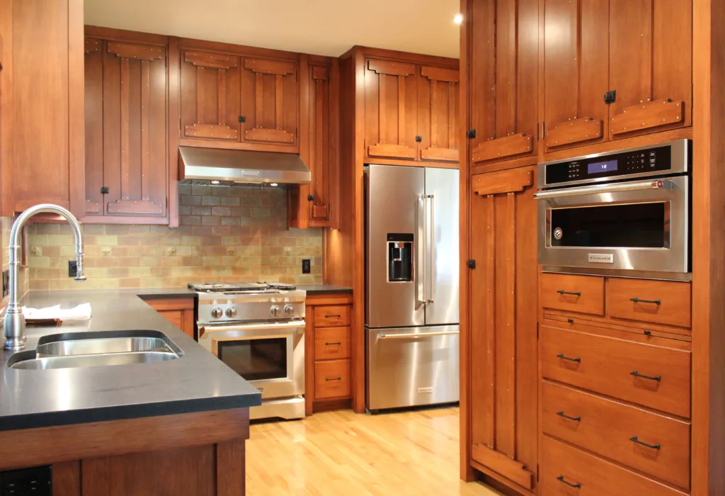 Remodeled Craftsman-inspired kitchen with stained wood cabinetry, stainless steel appliances, dark stone countertops, and green backsplash tiles