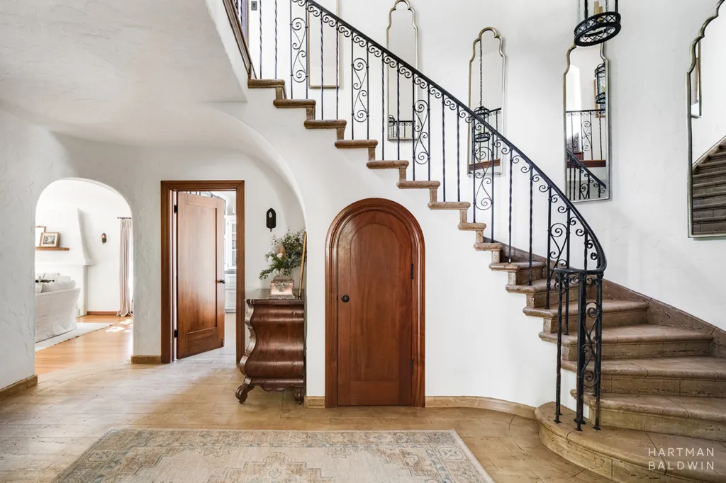 Spanish-style entry and curved staircase with wrought-iron accents and decorative mirrors