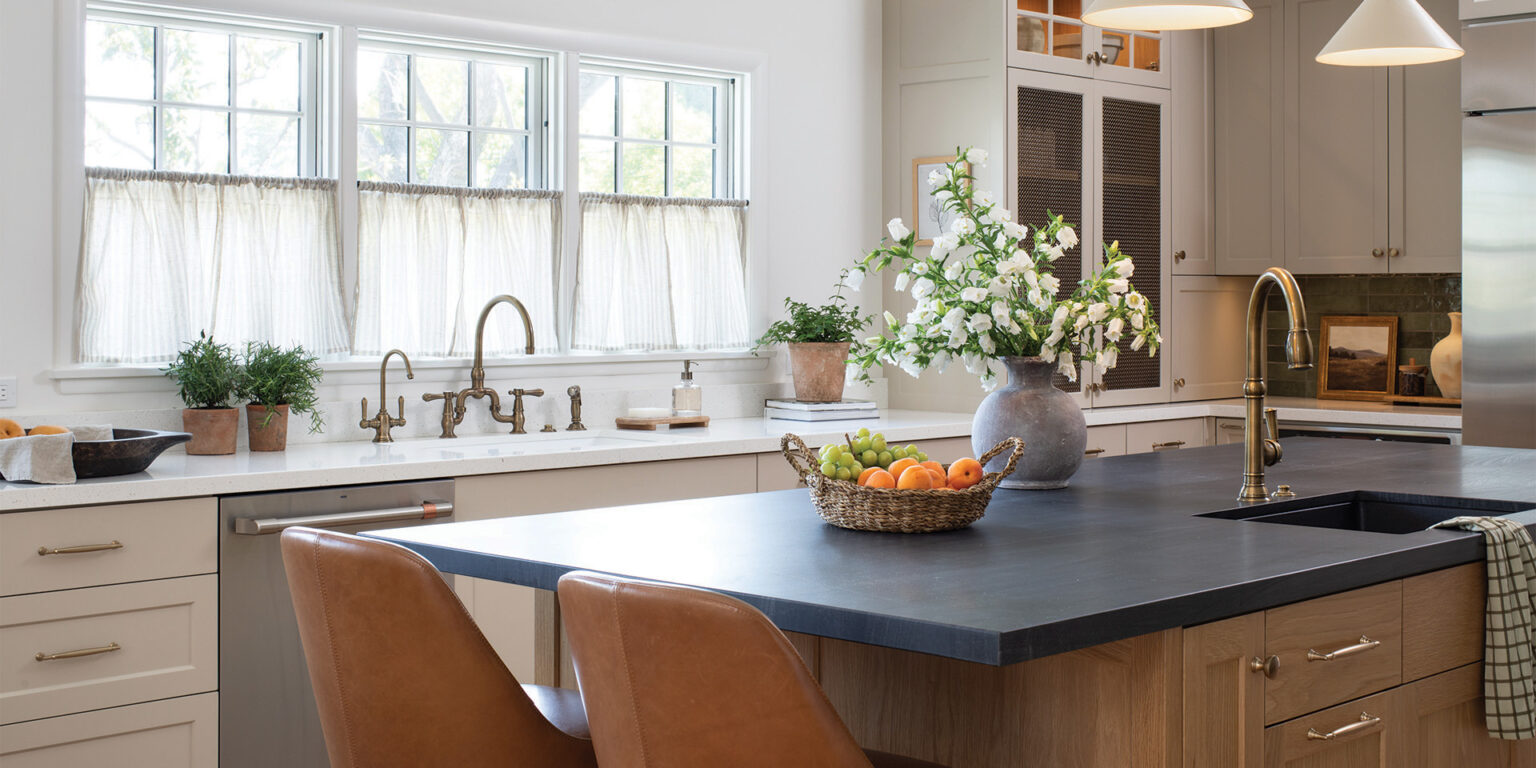 Contemporary kitchen remodel including central island with bar seating, stained wood cabinetry, dark stone countertop, and brass hardware
