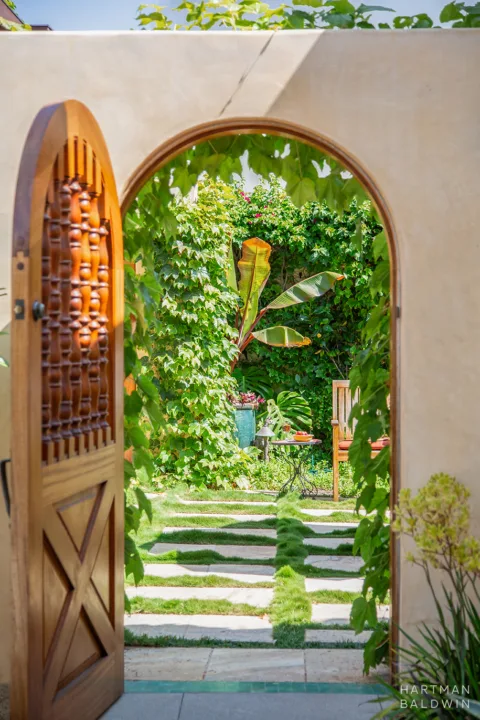 New stucco garden wall with a wooden gate open to a lush green backyard