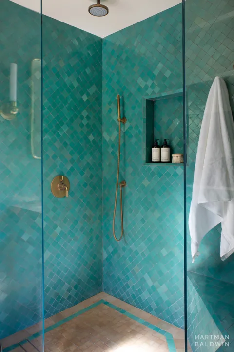 Bathroom shower with turquoise wall tile, niche shelf, and antique brass showerhead, handle, and hand sprayer