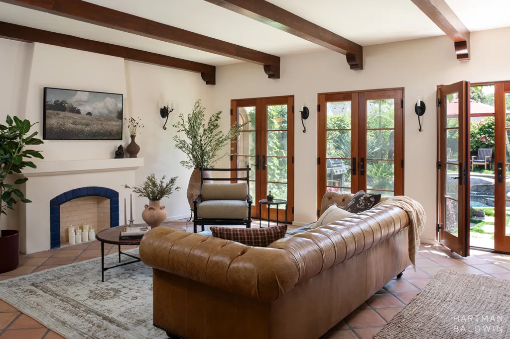 Remodeled Spanish-style living room with faux fireplace, stained wood French doors and ceiling beams, and large leather couch