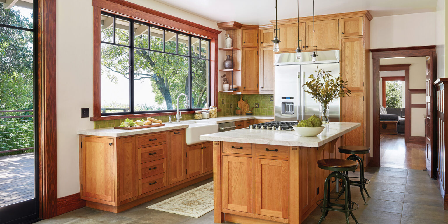 Remodeled Craftsman-style kitchen with light stained wood cabinetry, green tile backsplash, light stone countertops, and a large window above the sink