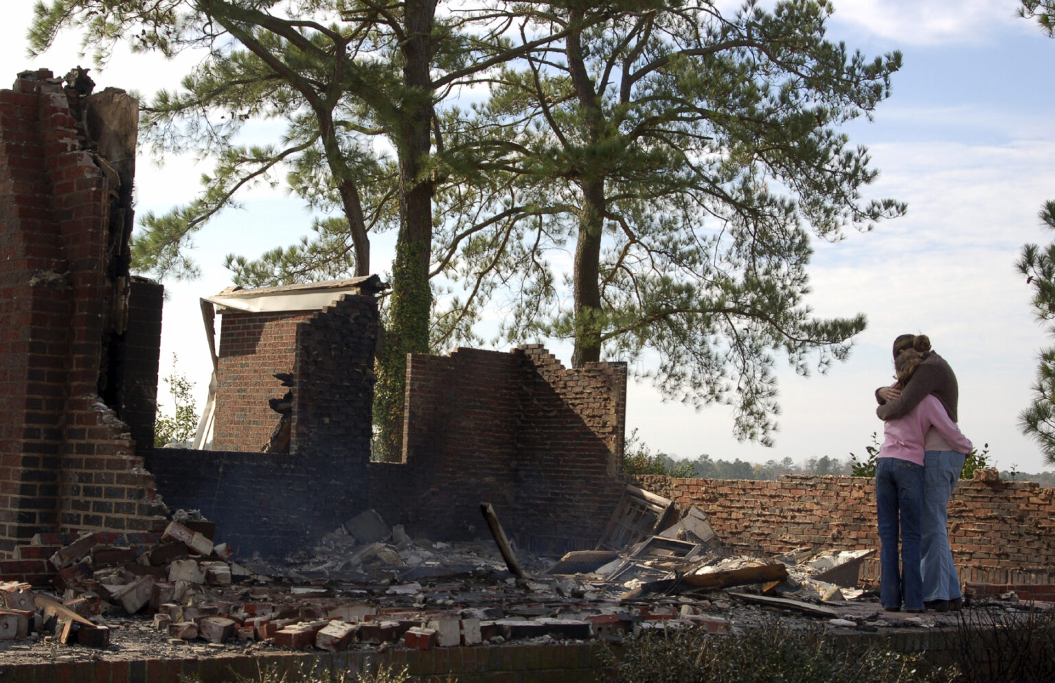 Couple hugging in front of burned-down home