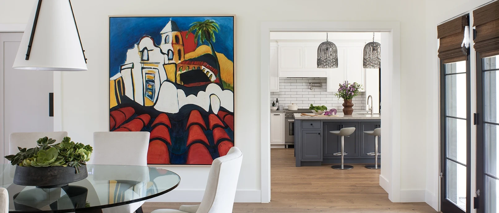 New custom modern dining room with a large colorful painting on the wall and the kitchen with white and blue cabinetry seen beyond