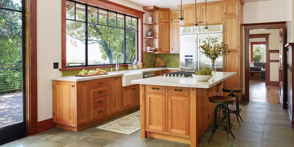 Remodeled Craftsman-style kitchen with light stained wood cabinetry, green tile backsplash, light stone countertops, and a large window above the sink