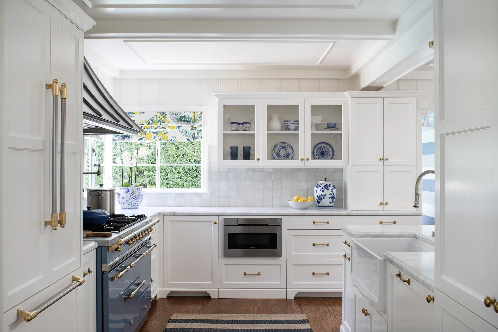 HartmanBaldwin 10th Street Residence Kitchen Detail - Hartman Baldwin Remodeled Cape Cod-style kitchen with white cabinetry, quartz countertop, aged brass hardware, farmhouse sink, and blue French Lacanche range