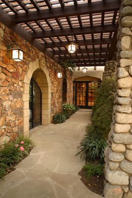 HartmanBaldwin Pomello Residence Guest House Corridor Corridor lined with wooden trellis, stone walls and columns and English garden landscaping leading from the primary home to the cottage guest house on English Tudor-style California estate