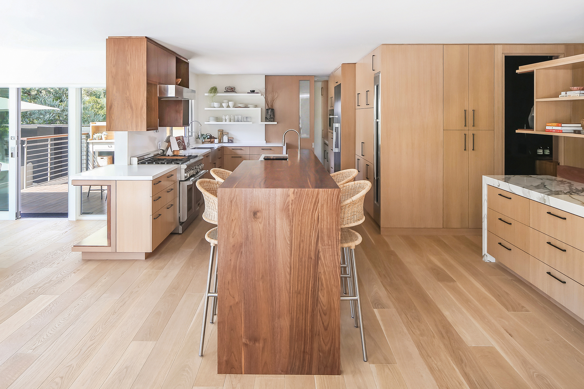 Large remodeled modern kitchen with waterfall-edge walnut island with bar seating, floating shelves, and quartzite buffet-style cabinet with dramatic multicolored veining