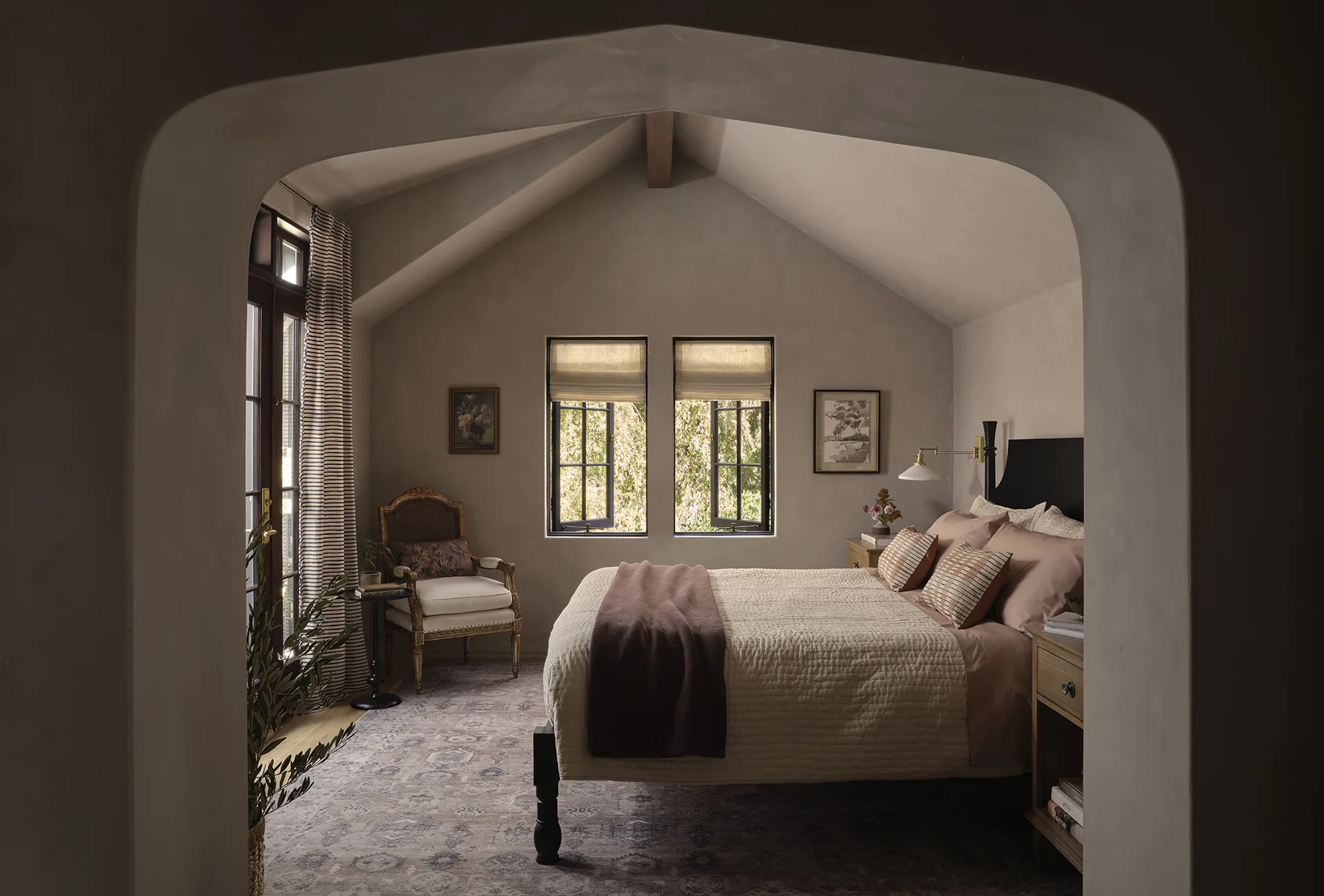 Cozy bedroom seen through an arched doorway, featuring a large bed with blush bedding and layered pillows.