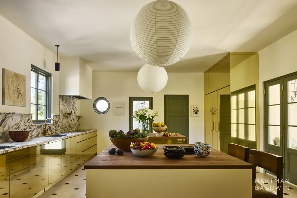 Bold luxury kitchen with reflective brass cabinetry, wood island countertops, stone perimeter countertops and backsplash with dramatic veining, and oversized sphere hanging paper lamp shades