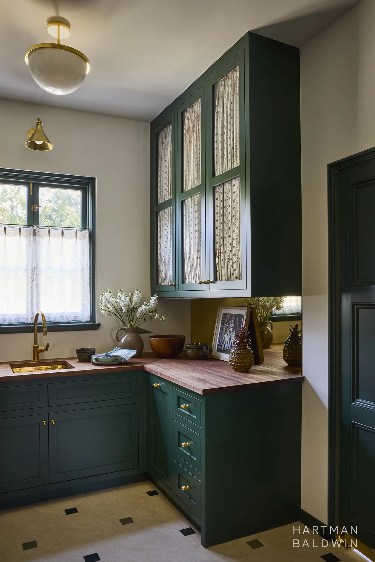 Luxury pantry with vibrant dark-green painted cabinetry, wood countertops, and gold-tone sink, faucet, cabinet hardware, and lighting pieces.