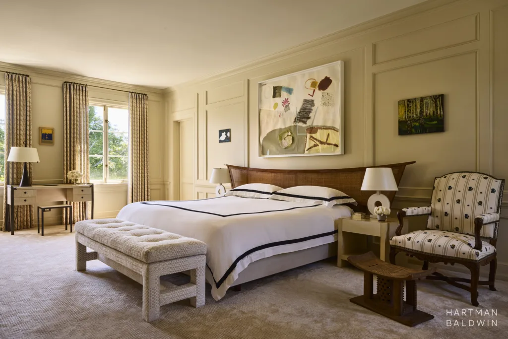 Primary bedroom with butter yellow paneled walls, bed with George Nakashima wood headboard, historic furnishings, and abstract art pieces.